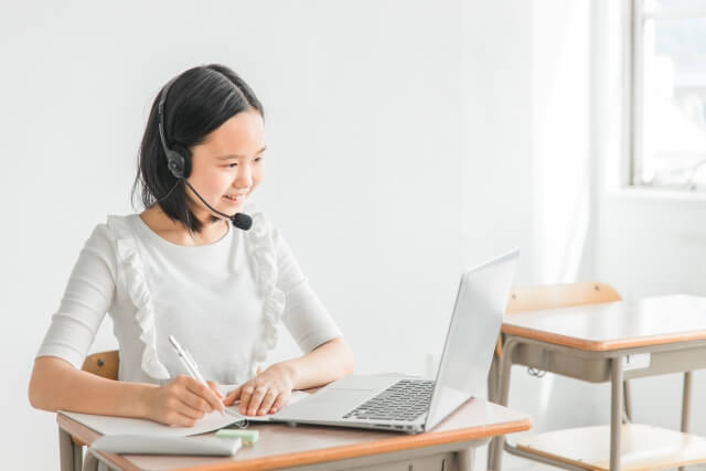 ヘッドセットをした女子学生がメモを取る