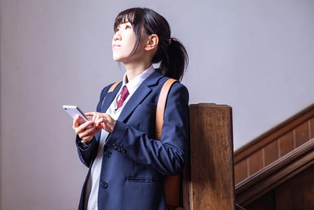 階段でスマートフォンを持つ女子学生